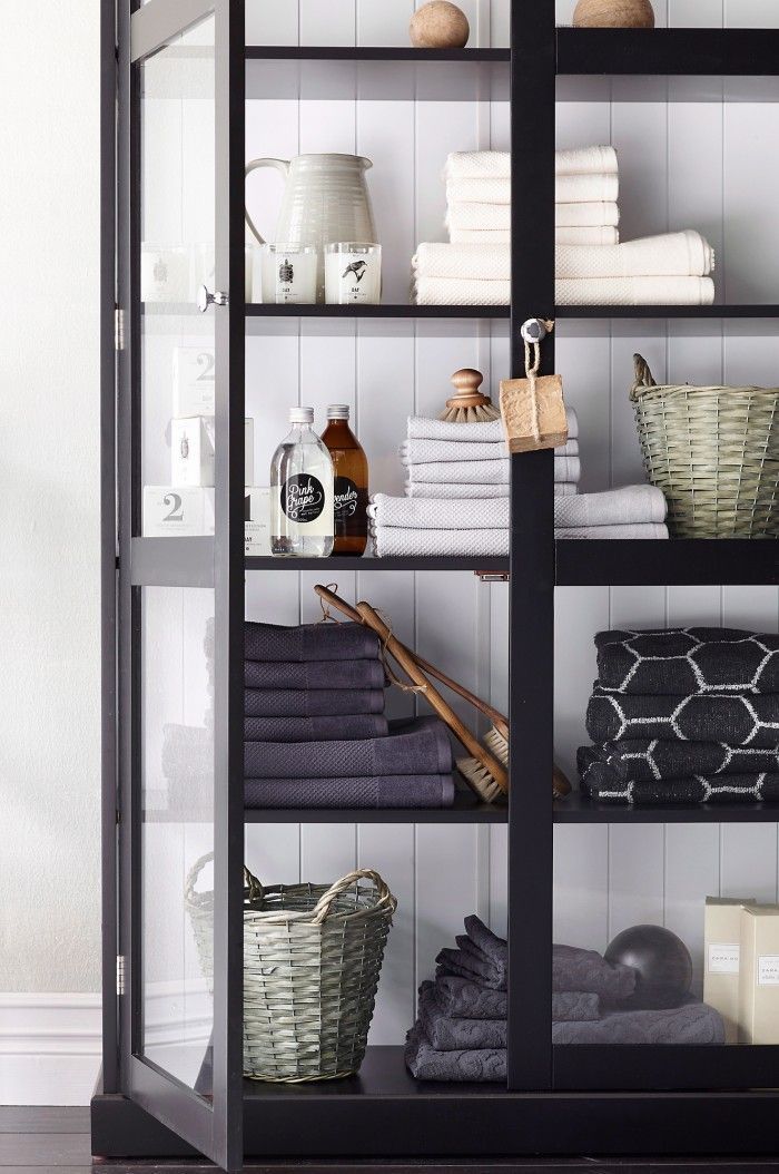 black cabinet with glass doors and styled shelves with piles of towels and baskets