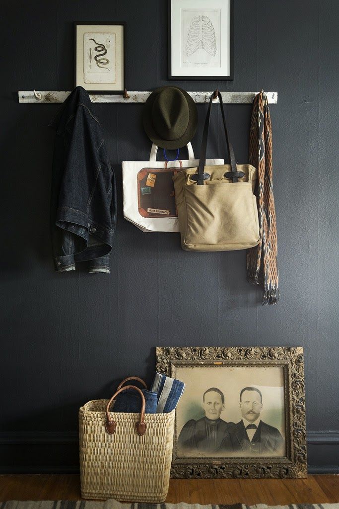Entryway vignette with dark monochrome walls, hanging weathered wood pegs, basket and a vintage portrait