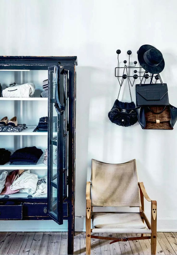 Vignette with chippy black cabinet, low slung chair and rack with hats and purses