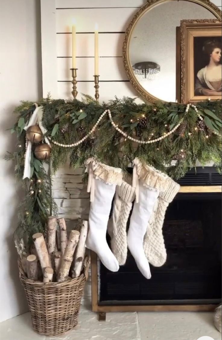 Christmas mantle with overflowing fresh greenery, tiny white lights, oversized jingle bells, cable knit stockings and wicker basket filled with birch wood