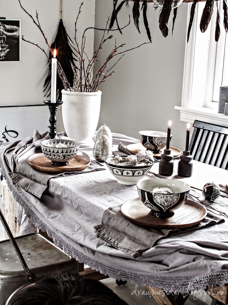 Bohemian table styled with candles, linen tablecloth, white urn with bare branches, black and white pottery and wooden chargers