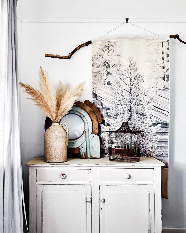 White winter tapestry with chipped white armoire and old vase of pampas grass