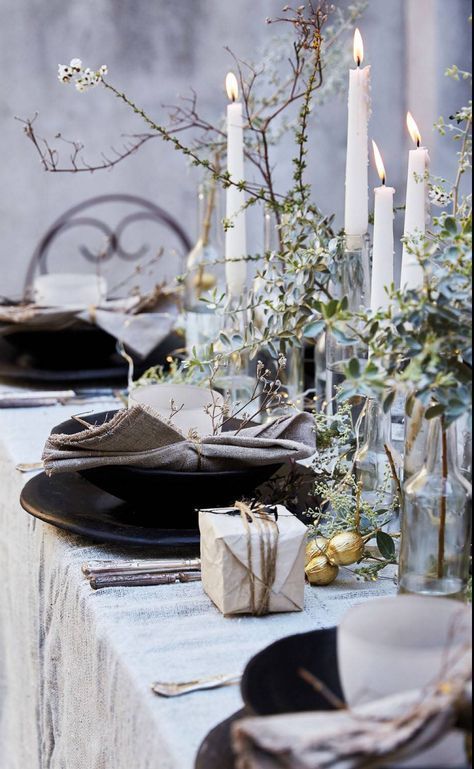 Beautiful holiday tablescape with flowering greenery, white taper candles, velvet napkins and tiny gifts wrapped with twine