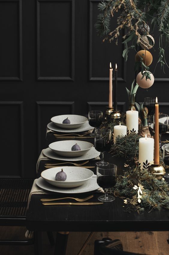 Holiday tablescape with black walls, greenery and peach taper candles with gold flatware