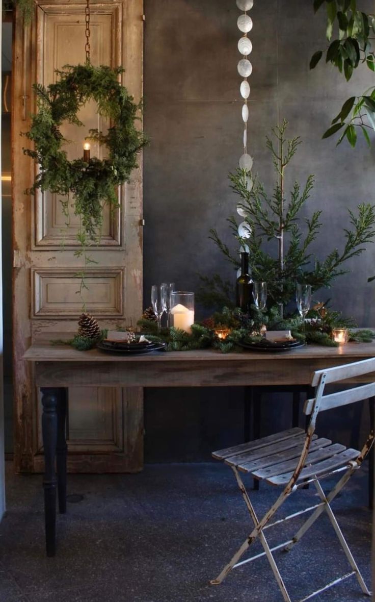 Simple holiday tablescape with wooden armoire and wreath with lighted candle in background, tinsel and glowing white candles