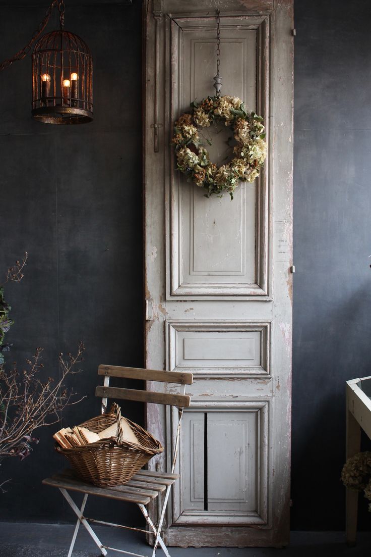 Chippy white wooden door leaning against wall with dried flowr wreath and bistro chair with basket of linen napkins
