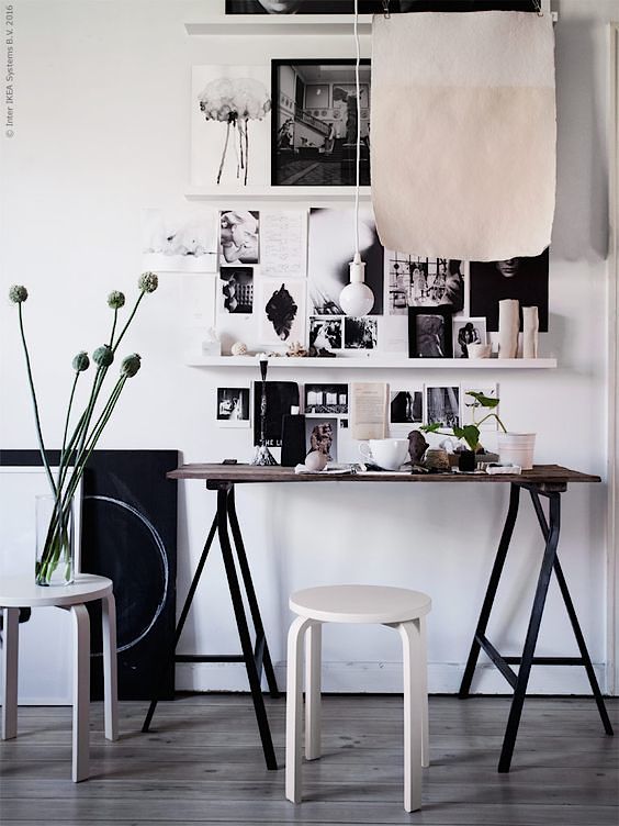 Gallery wall with black and white photos, architectural desk with small white stool and vase of simple modern flowers