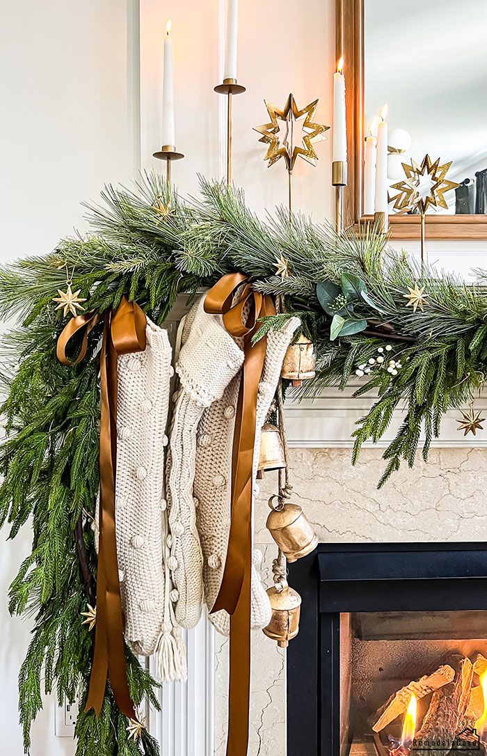 Close up of white sweater knit stockings on a mantel with brown satin ribbon and pine garland