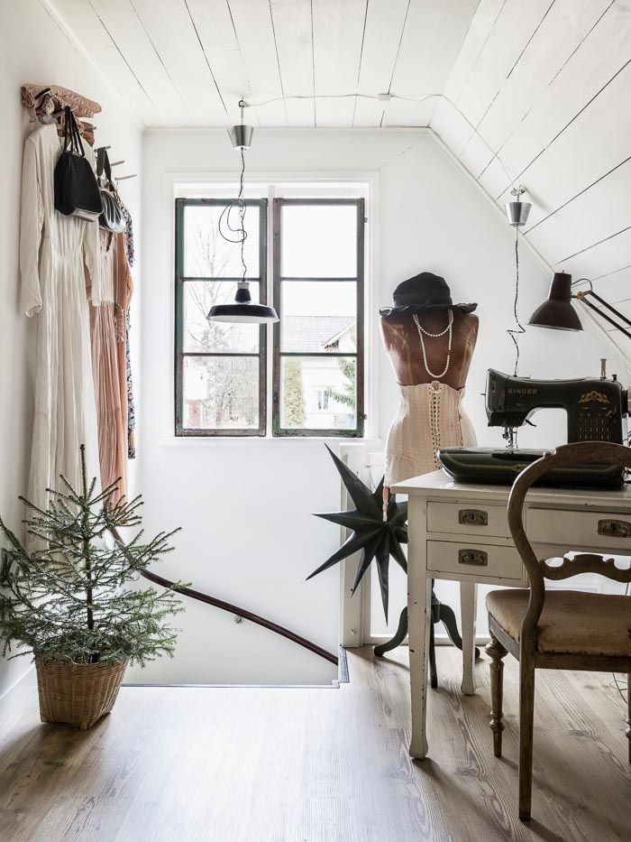 White atelier with mannequin and hanging clothes and old fashioned sewing machine on wooden desk and tiny fir tree on the floor