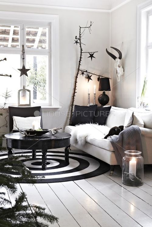 Beautiful Nordic living room with black and white round rug, white wooden floors and metal star hanging from windowsill