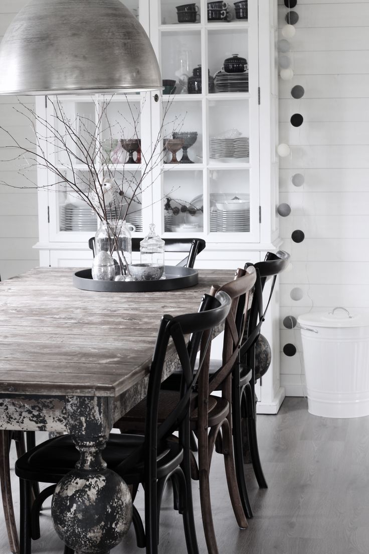 Elegant Scandinvian dining room with weathered wooden table, oversized silver lighting fixture and vase of branches on table