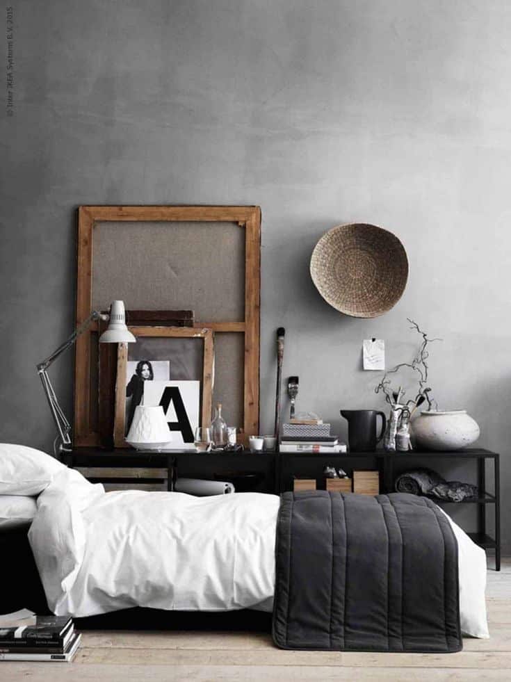 Chic bedroom with concrete walls, empty wooden picture frames ion wall and low bed on floor with white sheets and smoke velvet duvet