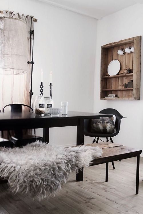 Simple dining room with wooden bench with flokati throw and rustic wooden wall shelf with white plates