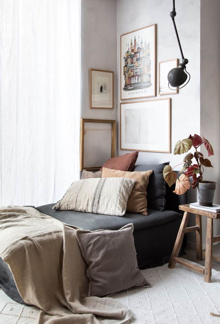 Corner of a bedroom with bed covered with velvet blue duvet and light framed prints above bed