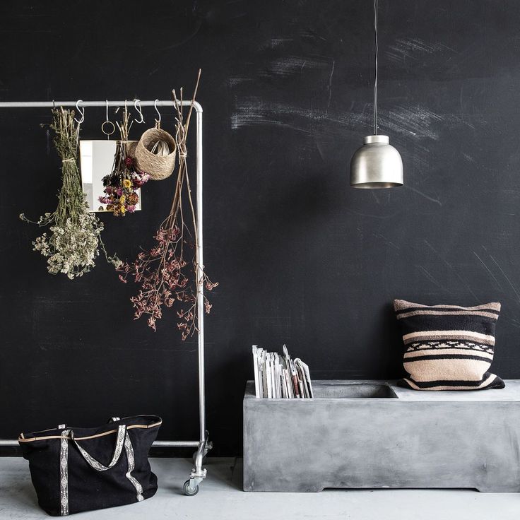 Chalkboard wall with white wire coatrack with hanging dried flowers and tote bag next to concrete settee with kilim pillow