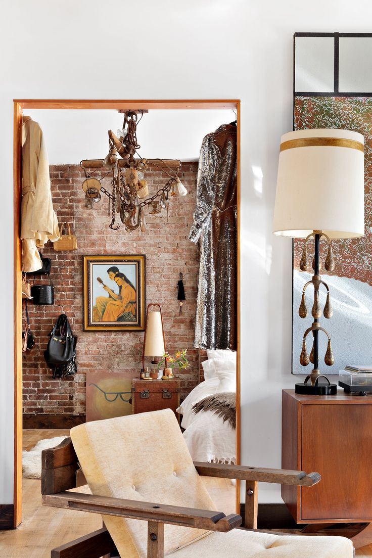 Beautiful loft with exposed brick walls, chandelier and vintage art in background, foreground with mid-century modern chest and eclectic vintage lamp