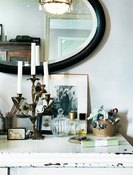 Tabletop display of vintage items including perfume bottles and brass candlesticks under a round mirror in black frame