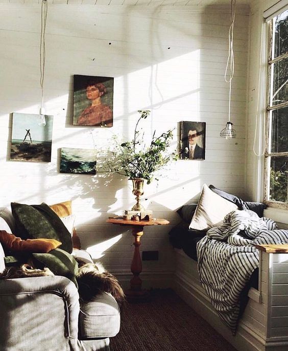 Light bright sunroom with daybed covered with pillows and throws and antique portraits