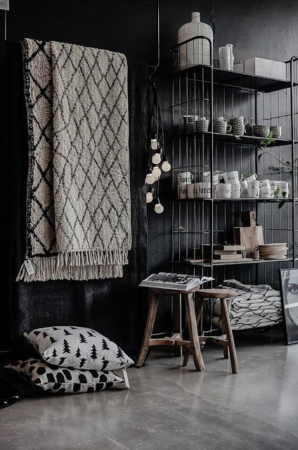 Room with black walls and shiny concrete floors with berber rug hanging on the wall and black wire shelf with white transferware
