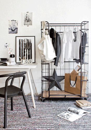 White room with black wire standing shelf with hanging clothes, a metal star and black and white gallery wall