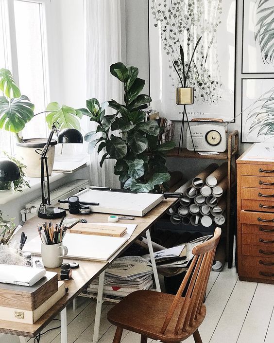 Cozy artist's workspace with natural light, featuring an organized wooden desk, vintage radio, and lush green plants.