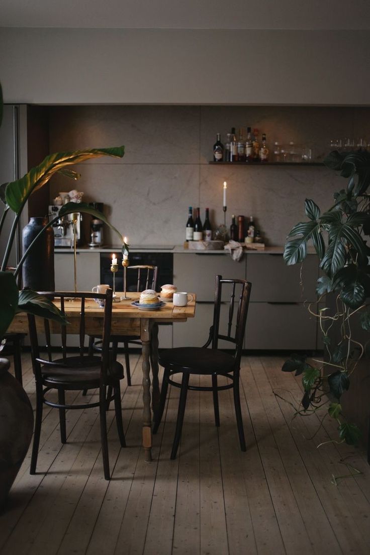 Dark and cozy kitchen with simple chairs and candles on table with standing pots of greenery