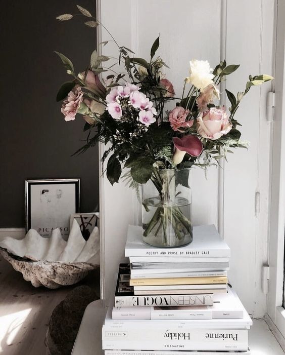 A vase of flowers atop a stack of books by a white door.