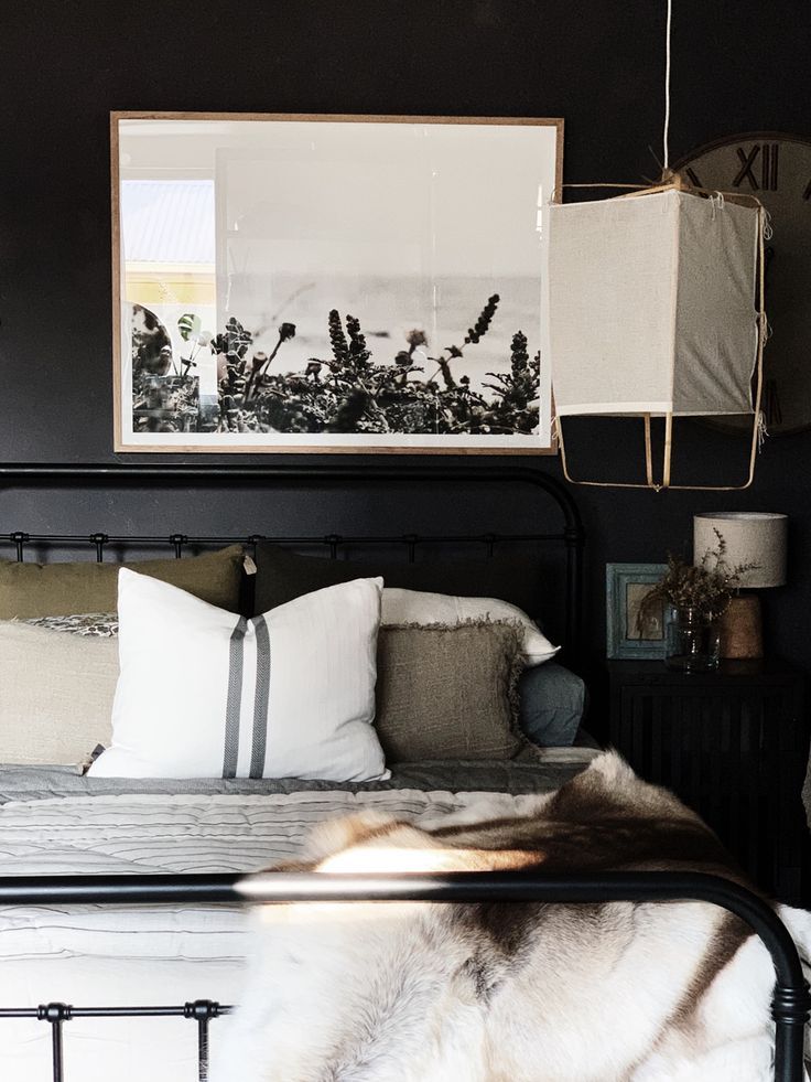 Elegant bedroom with monochromatic decor featuring a dark wall, framed artwork, a metal bed frame with pillows, and a fur throw.