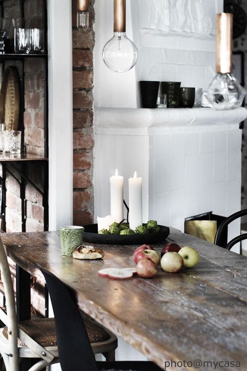 Rustic dining setting with exposed brick, a simple wooden table, and candles, evoking a cozy atmosphere.