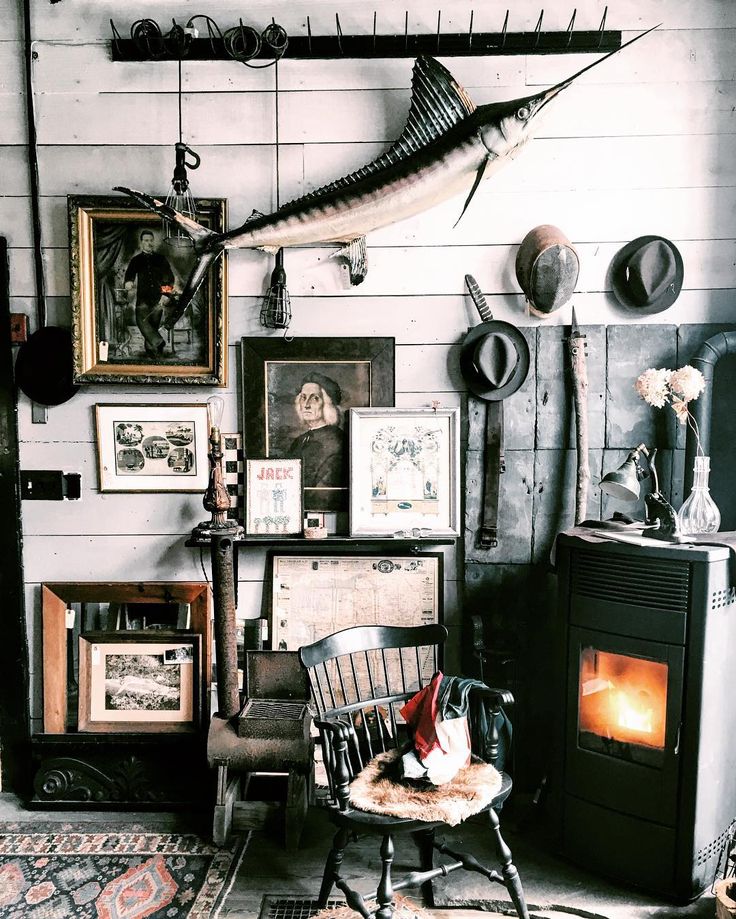 A cozy vintage interior with eclectic wall decor, including a mounted marlin, assorted paintings, and a warm fireplace.