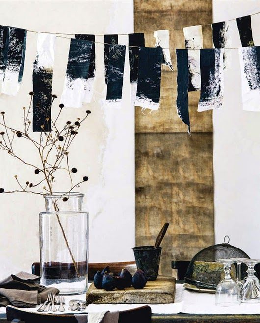 A festive dining setup with navy and white fabric bunting hanging above a rustic table adorned with dried flowers, vintage dishes, and glass jars. The decor exudes a charming and eclectic vibe perfect for a summer gathering.