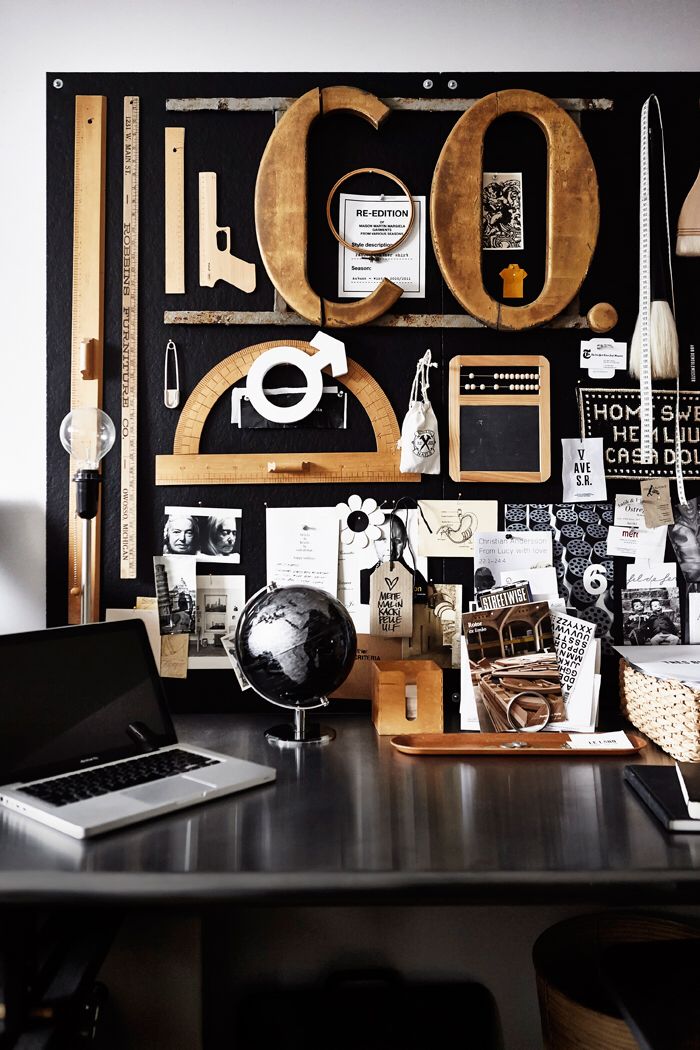 A creative workspace featuring a moodboard with eclectic elements including rulers, geometric shapes, vintage photos, and a globe. The desk below is equipped with a laptop, adding a modern touch to the vintage-inspired decor.