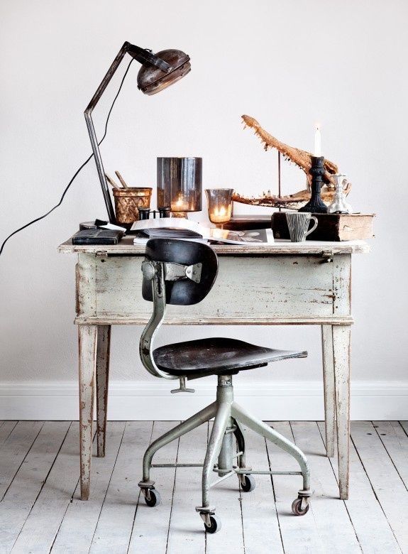 A rustic home office setup with a wooden desk, a vintage metal chair, and a large window allowing natural light to flood the space. The desk features a stylish lamp, a small plant, and a few neatly organized accessories.