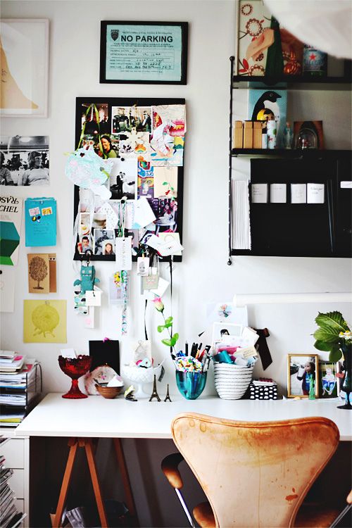 A chic home office with a black vintage desk placed under a large, empty gold frame on the wall. Inside the frame, a wire is used to hang various small pieces of art and notes, complementing the overall elegant and creative design.