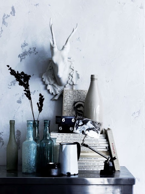 Rustic console table styled with vintage decor, including a lamp, horn, abstract art, and a distressed birdcage. The arrangement highlights neutral tones with subtle pops of color in the surrounding artwork and textiles.