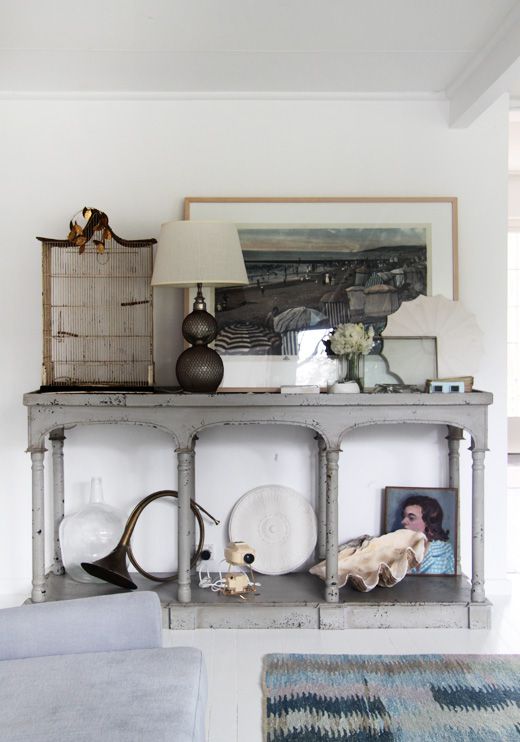 Industrial-style vignette with a white stag head mounted on the wall, surrounded by glass bottles, stacked books, and minimalist decor in neutral tones. The setup includes a vintage desk lamp and a letter board for added texture.