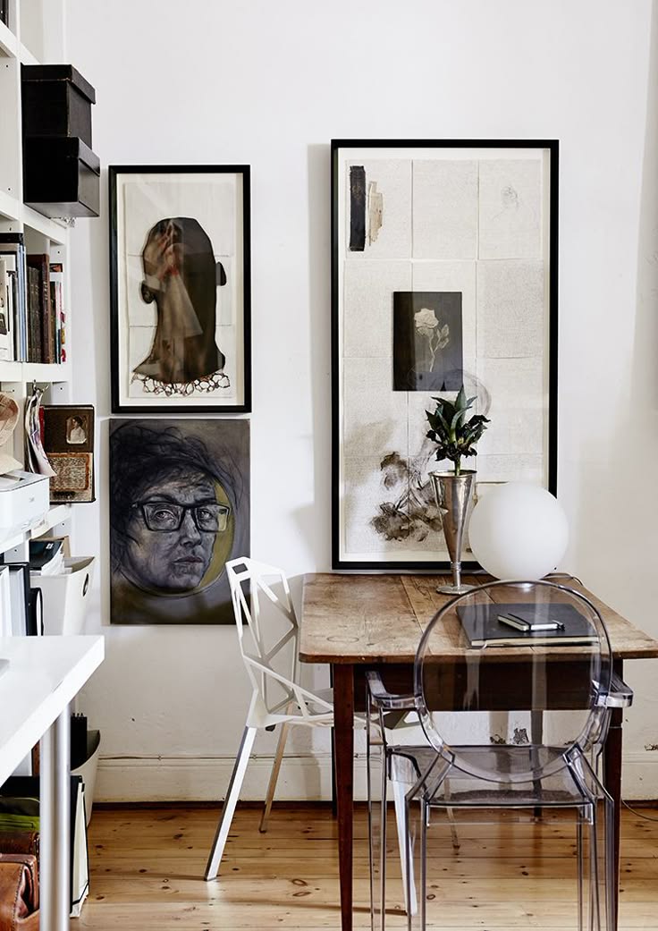 A home office with a dark wooden desk styled with a black and white striped pillow and decor, set against a gallery wall of eclectic framed portraits, sketches, and abstract art. The portraits feature various artistic styles and are arranged in a cohesive display, adding a personal touch to the workspace.