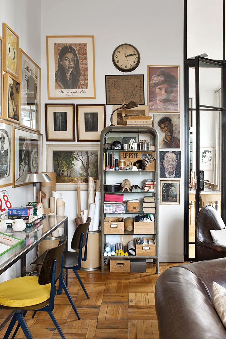 An industrial-style home office with metal shelving, framed artwork, and an assortment of books and decorative objects showcasing a curated cluttered space