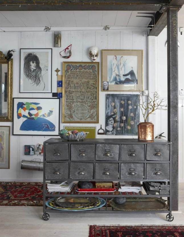 A gallery wall with an eclectic mix of artwork, vintage-style metal storage unit, and decorative objects creating an artistic, cluttered aesthetic.