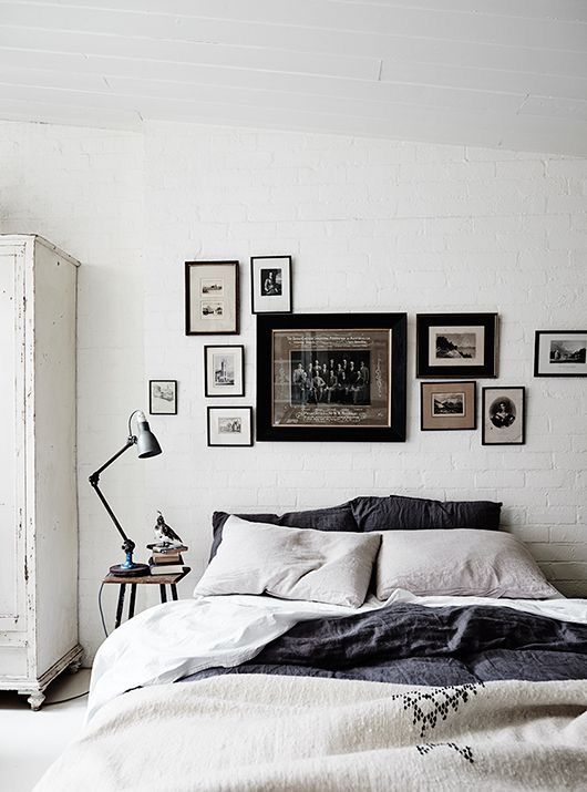 Minimalist gallery wall with black-and-white framed photos above a bed in a neutral-toned bedroom, creating a cohesive, vintage-inspired look on a white brick wall