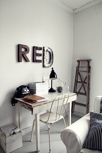Cozy home office corner with a rustic white desk, vintage telephone, and metal letters spelling ‘RED’ on the wall. An old wooden ladder leans against the wall, adding character to the minimalist space filled with black and white accents.
