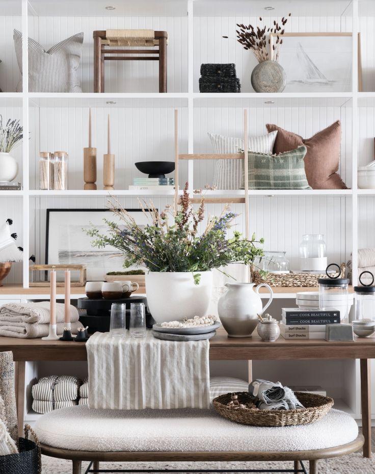 Beautifully styled open shelving filled with neutral decor items, including woven baskets, ceramic vases, and pillows. The arrangement features a mix of textures like linen, wood, and greenery, creating a serene, cozy atmosphere in a modern rustic style
