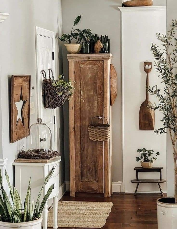 Rustic entryway corner featuring a tall wooden cabinet, woven baskets, potted plants, wooden wall decor, and natural textures like jute rugs and vintage accessories, creating a warm, inviting atmosphere.