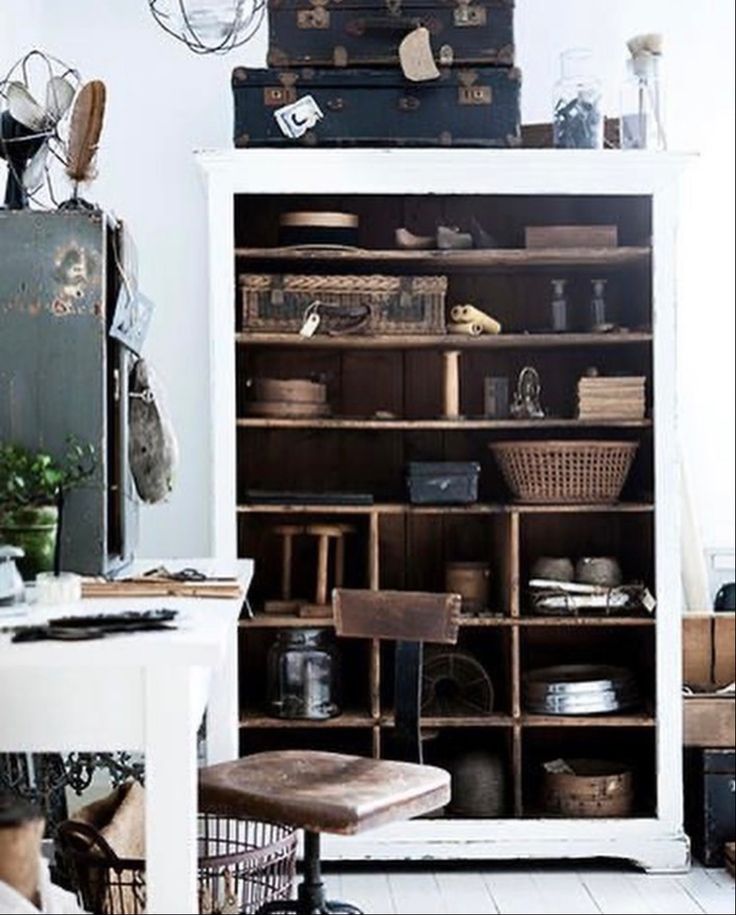 Industrial-inspired shelving unit filled with vintage suitcases, baskets, and collectibles in a workspace with a rustic chair, creating a warm and creative atmosphere.