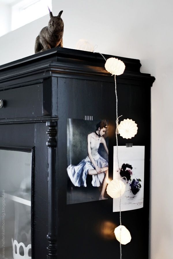 A black cabinet topped with a decorative rabbit figurine and adorned with soft, glowing string lights and pinned artwork, creating a moody and eclectic aesthetic.