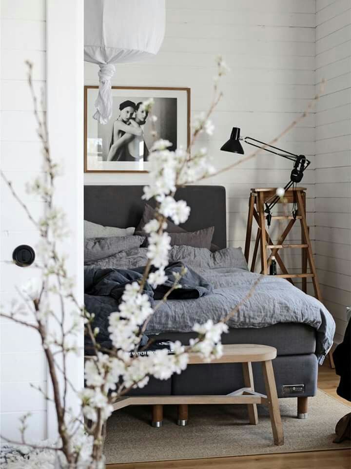 A cozy bedroom with soft gray bedding, framed black-and-white art on the wall, and a blooming branch in the foreground, adding a natural, bright touch to the space.