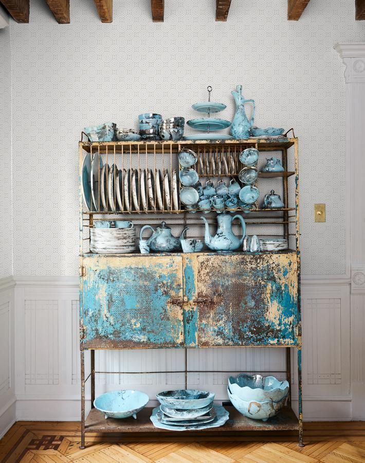 Rustic, industrial-style metal hutch with a weathered blue finish, showcasing a collection of vintage blue ceramic dishes. The hutch features open shelving filled with plates, bowls, and teapots, creating a curated display.