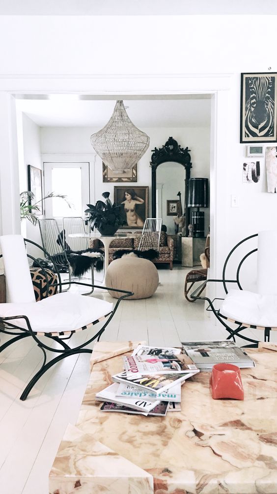 A bright, airy living room with white walls, featuring a mix of modern and vintage furniture, artwork, and a large beaded chandelier.