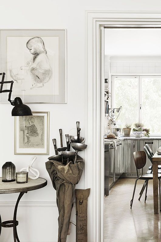 Example of bright white and weathered wood decor: white hallway with art and fencing gear, leading to a kitchen with gray weathered wood cabinets and white countertops.