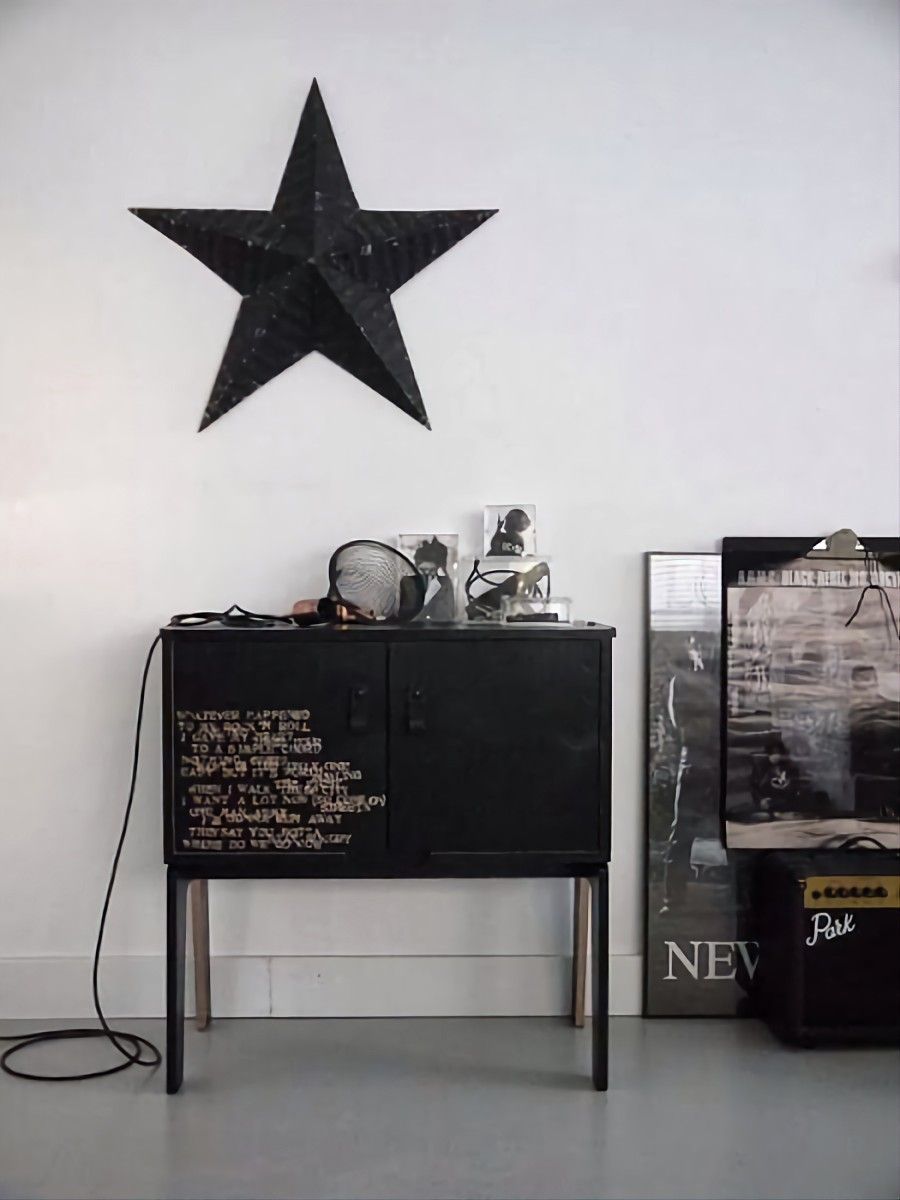 Black sideboard cabinet with stenciled rock-and-roll-inspired white typography, styled with a black star wall hanging, vintage posters, and an amplifier for an edgy, eclectic vibe.